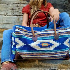 a woman sitting on the ground holding a large blue and white bag with southwestern designs