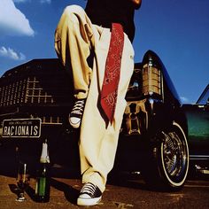 a man standing in front of an old car with his feet propped on the hood