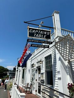 the captain's table sign is hanging from the side of an old white building