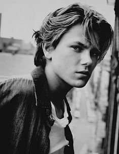 black and white photograph of a young man leaning against a wall with his head turned to the side