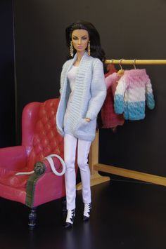 a barbie doll standing next to a pink chair and clothes on a rack in front of a black wall