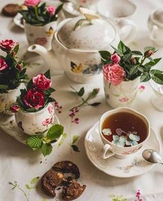 tea and cookies on a white table cloth with pink flowers in vases next to them