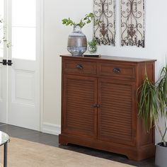 a wooden cabinet sitting next to a glass table with plants on it and two metal wall hangings