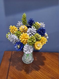 a glass vase filled with colorful flowers on top of a wooden table next to a blue wall