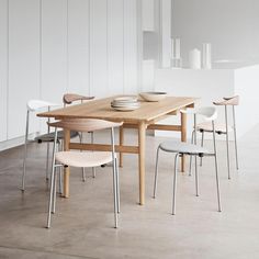 a wooden table surrounded by white chairs in an empty room with no one around it