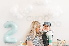 a woman holding a child in front of a table with balloons and letters on it