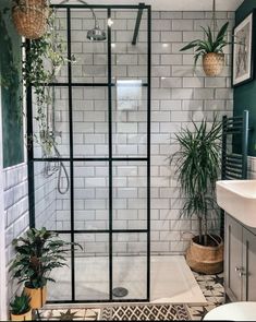 a bathroom with green walls and white tiles on the shower wall, plants in potted planters