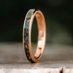 a wedding ring with green moss inlays on it sitting on a piece of wood