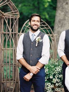 two men standing next to each other in front of a wooden structure with flowers on it