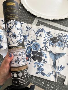 a person holding a bottle of paint next to some plates and napkins on a table