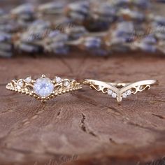 two gold rings sitting on top of a piece of wood next to some rocks and flowers