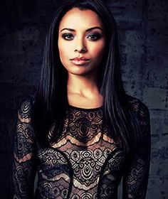 a woman with long dark hair wearing a black lace dress and posing for the camera