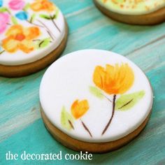 three decorated cookies sitting on top of a blue wooden table with flowers painted on them