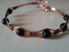 a close up of a bracelet on a white table with black beads and copper wire