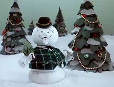 a snowman is standing in front of three christmas trees