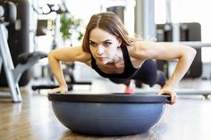 a woman is doing push ups on an exercise ball in the gym while looking at the camera