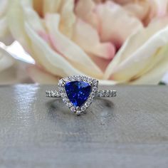 a diamond and blue sapphire ring sitting on top of a table next to a flower