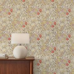 a lamp sitting on top of a wooden dresser next to a wallpaper covered in flowers