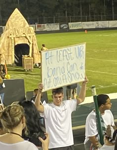 a man holding up a sign in front of a crowd at a football game on the field