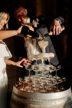 a bride and groom are pouring champagne into wine glasses on top of a wooden barrel