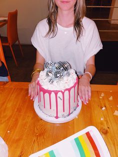 a woman sitting at a table with a cake in front of her and a rainbow striped plate