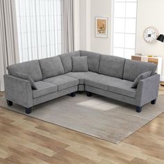 a gray sectional sofa sitting on top of a wooden floor next to a white rug