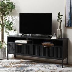 a flat screen tv sitting on top of a black entertainment center next to a potted plant