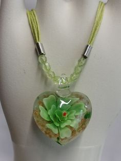 This is a hand blown glass heart pendant necklace. The heart has a green flower in the middle with gold glitter.  It has a lobster clasp for closure and hypoallergenic. This necklace has plastic beads where the pendant lays.                                                                                                                                               Please contact me with any questions or concerns. Handmade Green Jewelry For Valentine's Day, Green Adjustable Necklace With Flower Charm, Green Glass Pendant Jewelry, Green Pendant Flower Necklace As Gift, Green Pendant Flower Necklace For Gift, Heart-shaped Glass Necklaces For Jewelry Making, Green Heart-shaped Necklace For Gift, Green Heart Pendant Necklace As Gift, Green Heart Pendant Necklace Gift