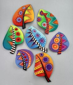 six brightly colored painted leaves on a white surface with dots and circles in the middle