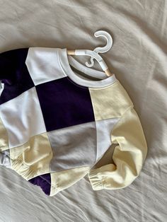 a white and purple sweater laying on top of a bed next to an umbrella shaped object