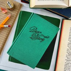 two green books sitting on top of a table next to some pens and pencils