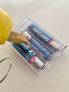 a pair of pencils and two batteries in a plastic container on a white table