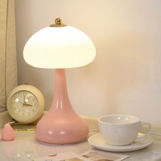 a pink lamp sitting on top of a table next to a cup and saucer