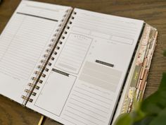 an open planner sitting on top of a wooden table next to a potted plant