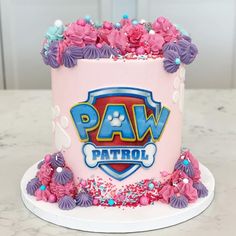 a pink cake with purple and blue frosting has paw patrol written on the side