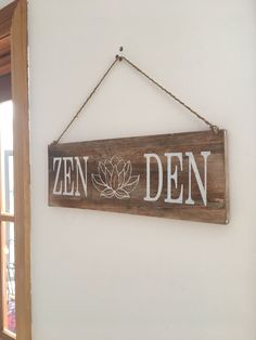 a wooden sign hanging from the side of a white wall next to a window with a potted plant on it