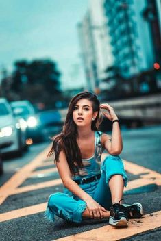 a young woman sitting on the side of a road next to a street with cars