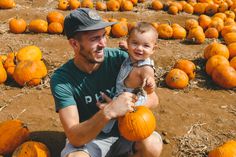 a man holding a small child in front of pumpkins