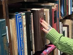 a woman's hand reaching for a book on a bookshelf filled with books