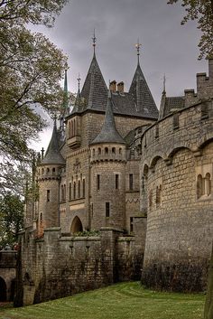 an old castle with turrets and towers on the top floor is surrounded by trees in front of a cloudy sky