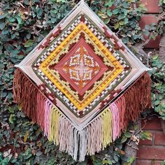 a wall hanging made out of different colors and fringes on top of a brick wall