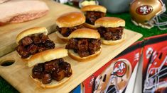 small sandwiches with meat on them sitting on a cutting board next to other food items