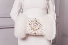 a woman wearing a white dress and fur stoler holding a purse with pearls on it