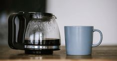 a coffee pot next to a cup on a table with water in the bottom and inside