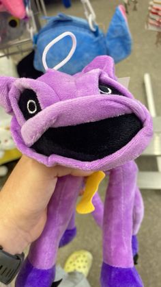 a purple dragon stuffed animal being held by a person's hand in a store