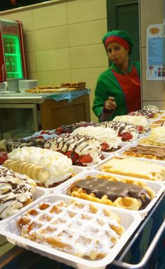 a woman standing behind a counter filled with lots of desserts