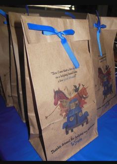 two brown paper bags with blue ribbons on them sitting on top of a blue cloth covered table