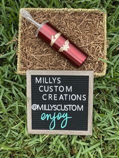 a sign that says millys custom creations and an empty bottle in the grass next to it