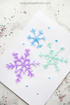 snowflakes made out of colored powder on top of a piece of paper with sprinkles