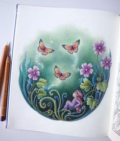 an open book with butterflies and flowers on the cover, next to two colored pencils